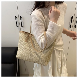 Detail of a large straw tote bag featuring natural beige texture and brown leather straps
