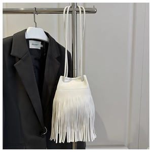 Detail shot of a white tassel bucket bag with pebble leather texture and thin shoulder straps