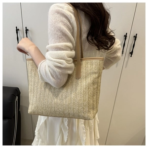 Detail of beige straw tote bag with brown leather straps shown on model's shoulder