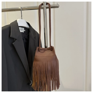 Detailed close-up of brown pebbled leather bucket bag featuring long fringe tassels