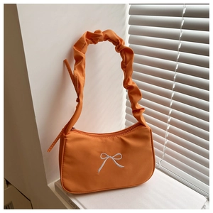 Détail du sac orange avec poignée froncée et broderie nœud blanc sur décor épuré