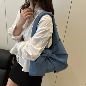 Blue denim hobo bag with large bow decoration shown on model for a trendy retro look
