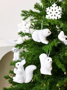 Primer plano de adornos de oso polar y ardilla flocados blancos colgados en un árbol de Navidad