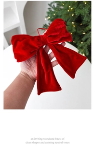 Detail of red velvet Christmas bow decoration held against a festive holiday tree
