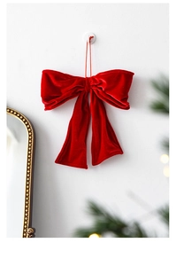 Detail of a large red velvet Christmas bow hanging on a white wall with festive pine decor