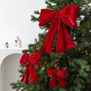 Set of three red velvet Christmas bows in various sizes hanging on a lit Christmas tree