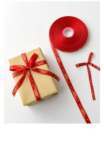 Rotes Weihnachtsband mit goldenem Merry Christmas Aufdruck auf Geschenkbox und Rolle