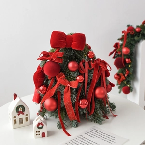 Mini tabletop Christmas tree with red velvet bows and ornaments on a white desk