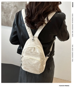 Detail of a minimalist cream-colored backpack showing its pleated texture and multi-pocket design