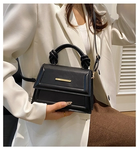 Close-up of black crossbody bag with gold bar detail and elegant knotted handle design