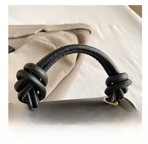 Close-up of black leather handbag featuring a knotted handle and gold metal eyelet detail