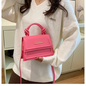Detail of a bright pink crossbody bag with a unique knot handle and gold buckle