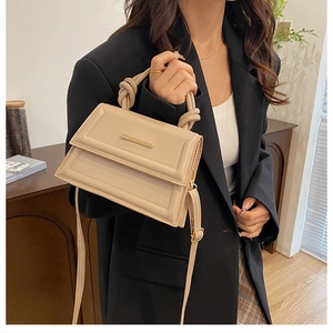 Detail of beige quilted leather handbag with knotted handle and gold metal bar accent