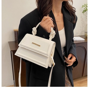 Detail of white leather handbag with knotted rope handle and gold metal trim hardware
