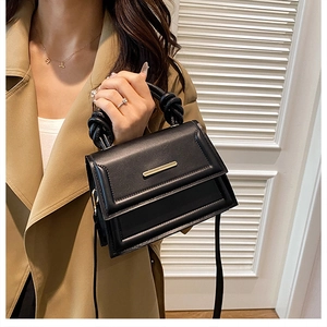 Detail of black crossbody bag featuring a twisted handle and gold bar accent