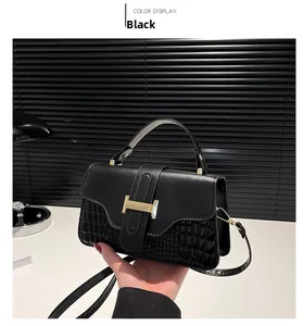 Close-up of black crossbody bag featuring faux crocodile texture and golden H-shaped clasp