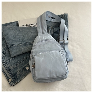 Detail of light blue wrinkled texture chest bag with zippers on a denim background