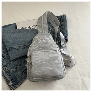 Detailed view of a silver sling bag with metallic crinkled texture on a minimal background