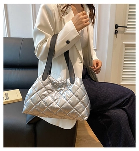 Close-up of shiny silver quilted tote bag with diamond stitching and black straps