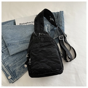 Detail of black nylon chest bag with multiple zipper layers and wide strap on white fabric