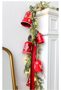 Detail of red Christmas bells with pine needles and velvet ribbon on a white fireplace