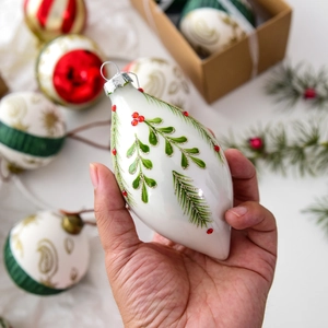 White teardrop Christmas glass ornament with green pine leaf pattern and red rhinestones