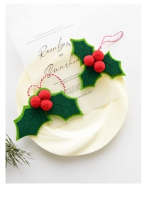 Detail of Christmas holly leaf ornaments with red berries and festive cords on a plate