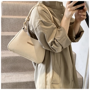 Detail of minimalist beige underarm bag with woven strap and gold bar on brown trench coat