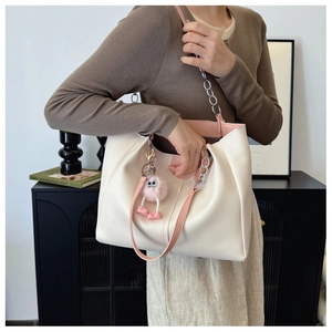 Large cream tote bag with pink straps and plush monster charm shown in a modern home setting