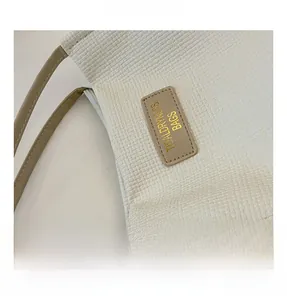 Detail of cream-white tote bag featuring textured 3D embossed grid and leather logo patch