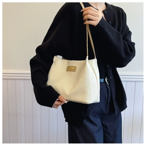 Detail of cream woven tote bag with brown leather brand tag worn on shoulder