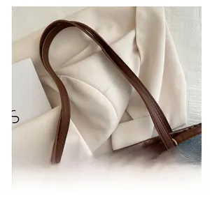 Dettaglio dei manici in pelle marrone e anelli dorati della borsa tote in denim