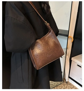 Close-up of brown vintage leather hobo bag with gold hardware worn over a black coat