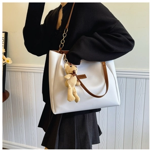 Close-up of white tote bag featuring brown straps, fashion logo, and a cute bear charm