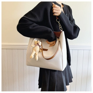 Detail of large tote bag with FASHION logo and cute beige knitted bear charm accessory