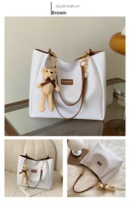 Detail view of a white leather tote bag with brown straps and a cute knit bear charm