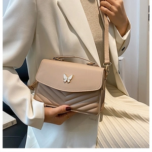 Détail du sac bandoulière abricot avec décoration papillon dorée et texture matelassée en V