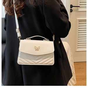 Détail d'un sac bandoulière blanc matelassé avec boucle papillon en métal sur modèle