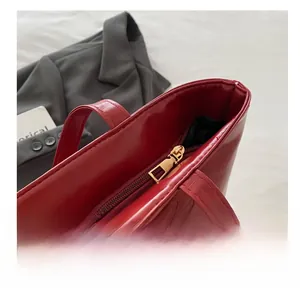 Close-up of smooth gold metal zipper on red glossy leather tote bag with clear texture