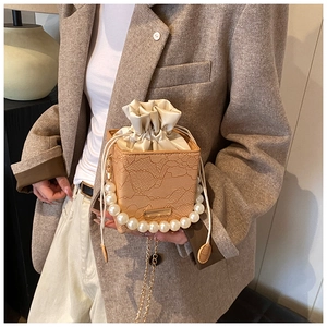 Detail of light brown box bag with lace texture, pearl handle, and gold chain strap