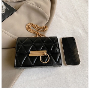 Close-up of quilted crossbody bag with gold chain strap and metal lock next to a smartphone