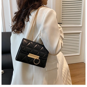 Detail of black quilted crossbody bag with golden chain strap and round metal buckle