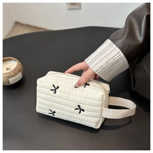 Close-up of white quilted cosmetic bag with black embroidered bows and side handle
