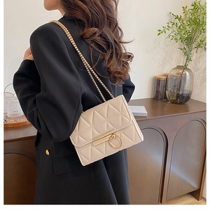 Detail view of quilted cream crossbody bag with gold ring buckle and chain strap on a model