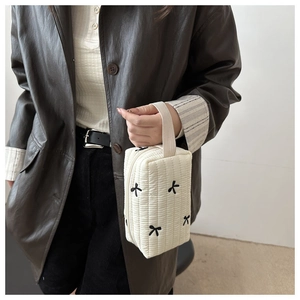 Macro detail of cream quilted hand bag with black embroidered bow and wide fabric handle