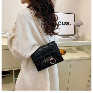 Close-up of black quilted small square bag with gold chain and large ring buckle