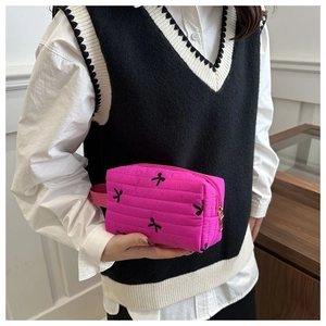 Detail of fuchsia quilted makeup bag with black bow embroidery and metal zipper