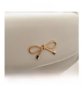 Close-up of golden bow metal buckle and fine stitching on white leather handbag