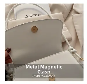 Close-up of the light gold magnetic clasp on a creamy white leather shoulder bag