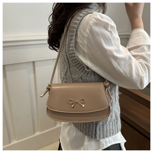 Detail of beige crossbody bag featuring a golden bow buckle and knotted strap design